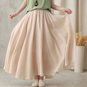 May include: A flowing, beige maxi skirt with a wide, gathered waistband. The skirt is made of a lightweight fabric that drapes gracefully. The hemline has a subtle, scalloped edge. The skirt is part of a casual outfit.