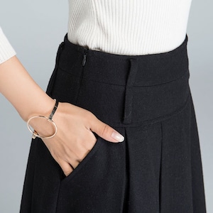 May include: A black high-waisted skirt with a zipper closure and pleats. The skirt is made of a soft, textured fabric.