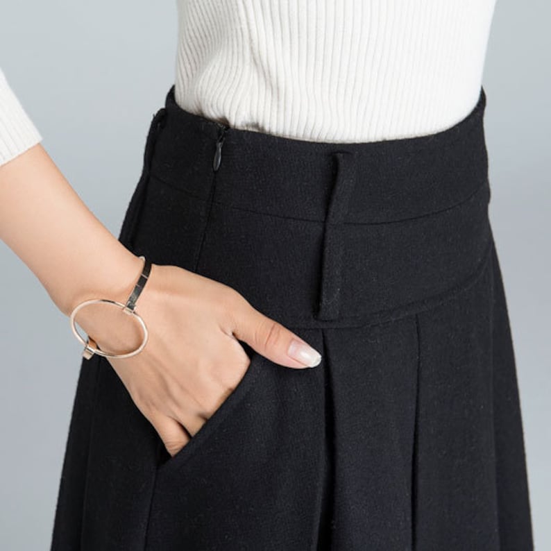 May include: A black high-waisted skirt with a zipper closure and pleats. The skirt is made of a soft, textured fabric.