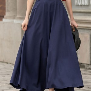 May include: A navy blue, full-length skirt with a wide, flowing silhouette. The skirt is paired with a red belt and a white top. The outfit is completed with black sandals and a black hat.