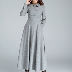Puede incluir: Un vestido gris de manga larga con cuello de Peter Pan y falda acampanada. El vestido tiene bolsillos a los lados.
