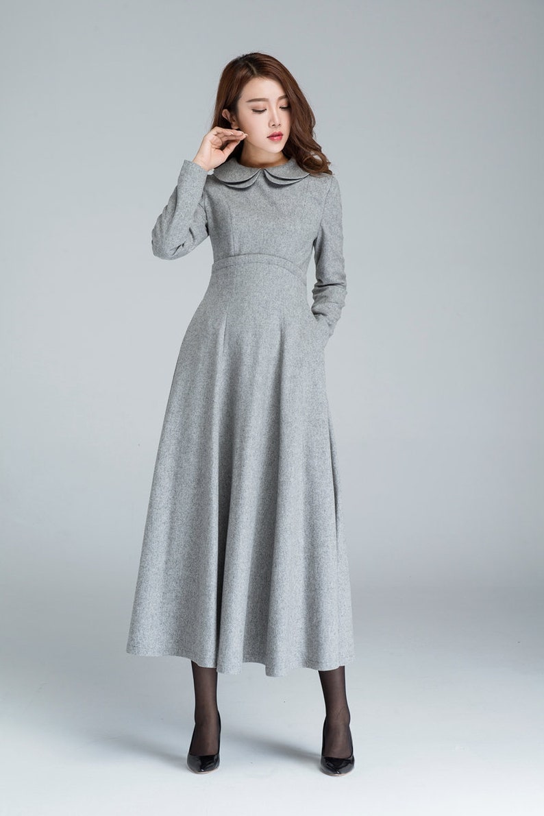Puede incluir: Un vestido gris de manga larga con cuello de Peter Pan y falda acampanada. El vestido tiene bolsillos a los lados.