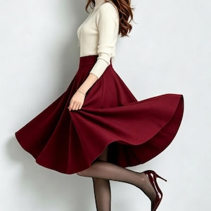 May include: A cream-colored long-sleeve mock neck top paired with a high-waisted, flared midi skirt in a deep burgundy red. The outfit is completed with sheer black tights and matching burgundy red pointed-toe high-heeled pumps.