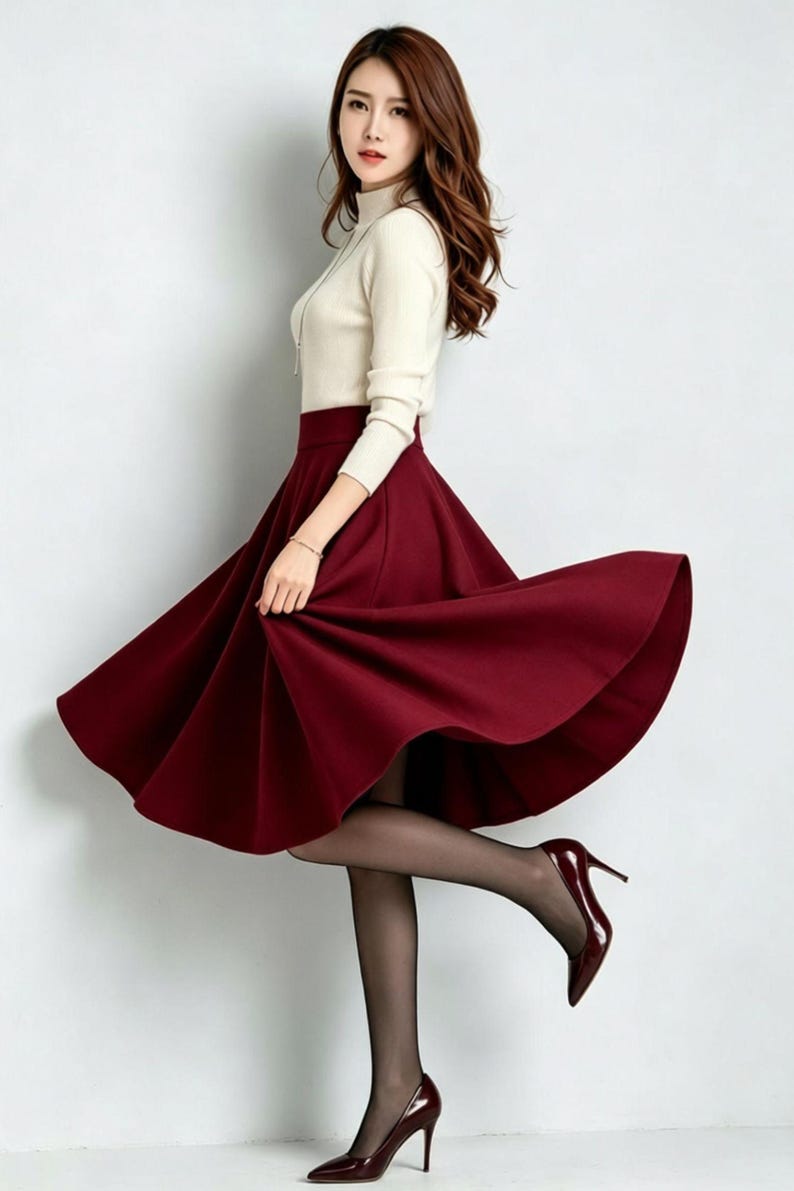 May include: A cream-colored long-sleeve mock neck top paired with a high-waisted, flared midi skirt in a deep burgundy red. The outfit is completed with sheer black tights and matching burgundy red pointed-toe high-heeled pumps.