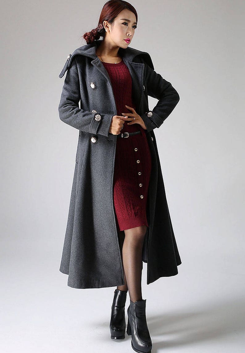 May include: A long, gray wool coat with a double-breasted closure and large buttons. The coat has a wide collar and a flared skirt.