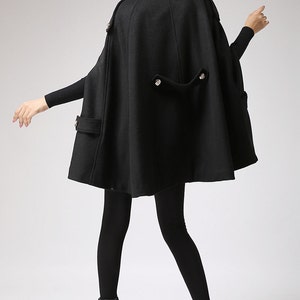 May include: Black hooded cape with a long, flowing design. The cape has a high collar and a button closure at the neck. The cape is made of a soft, warm fabric and is perfect for cold weather.