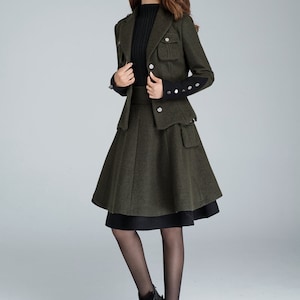 Puede incluir: Un traje de falda de lana verde con un jersey de cuello alto negro. La chaqueta tiene un dise&ntilde;o de inspiraci&oacute;n militar con botones y bolsillos. La falda es de l&iacute;nea A y llega a la rodilla.