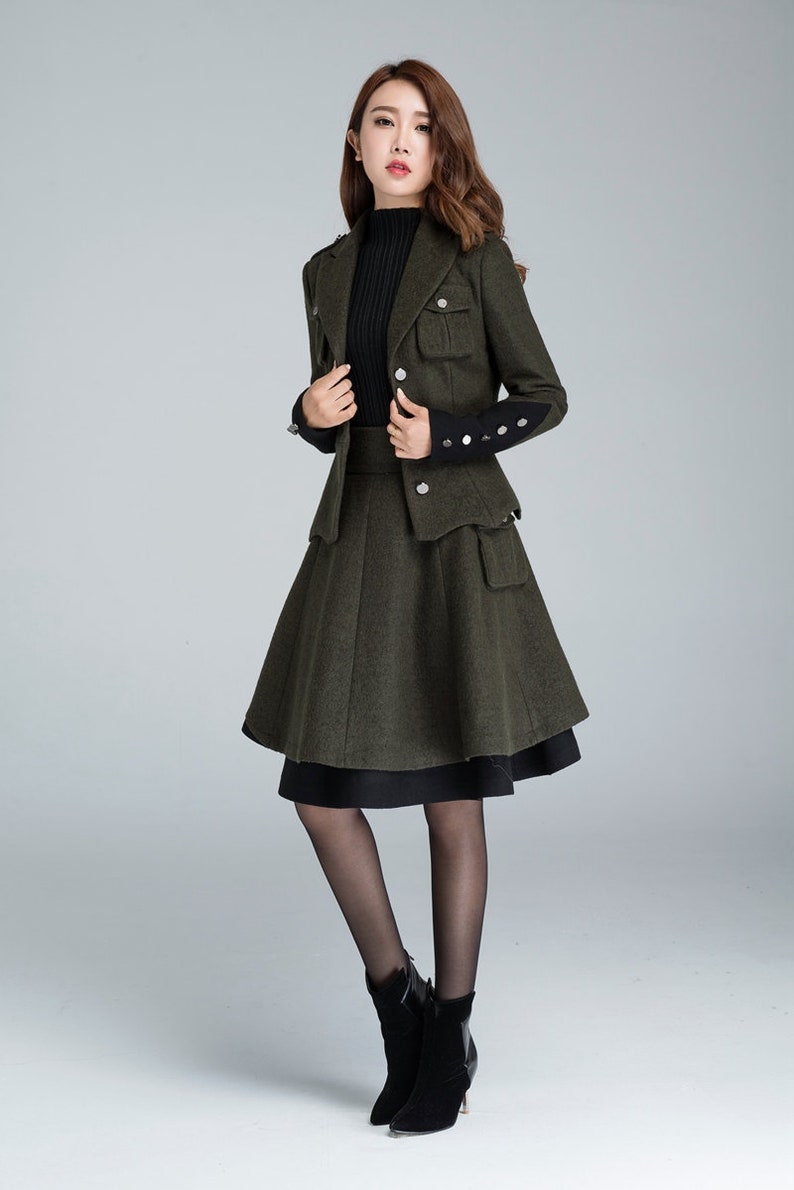 Puede incluir: Un traje de falda de lana verde con un jersey de cuello alto negro. La chaqueta tiene un dise&ntilde;o de inspiraci&oacute;n militar con botones y bolsillos. La falda es de l&iacute;nea A y llega a la rodilla.