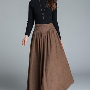 May include: A brown long skirt with a high waist and pleats. The skirt is made of a textured fabric and has a flowing silhouette.