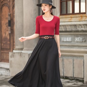 May include: A woman wearing a red scoop-neck top with elbow-length sleeves and a long black skirt. She is wearing a black hat and a brown belt with a gold buckle. The outfit is suitable for a formal event.