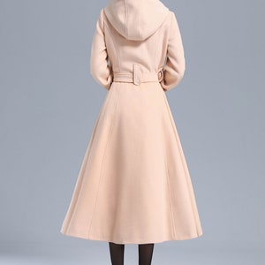 May include: A long, light pink hooded coat with a belt. The coat has a flared skirt and is made of a soft, warm fabric.