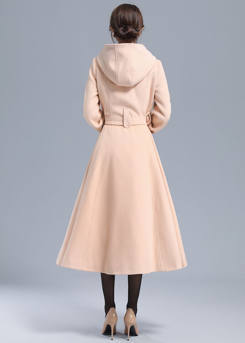 May include: A long, light pink hooded coat with a belt. The coat has a flared skirt and is made of a soft, warm fabric.