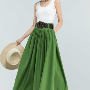May include: A green maxi skirt with a brown woven belt. The skirt is pleated and has a flowing silhouette.