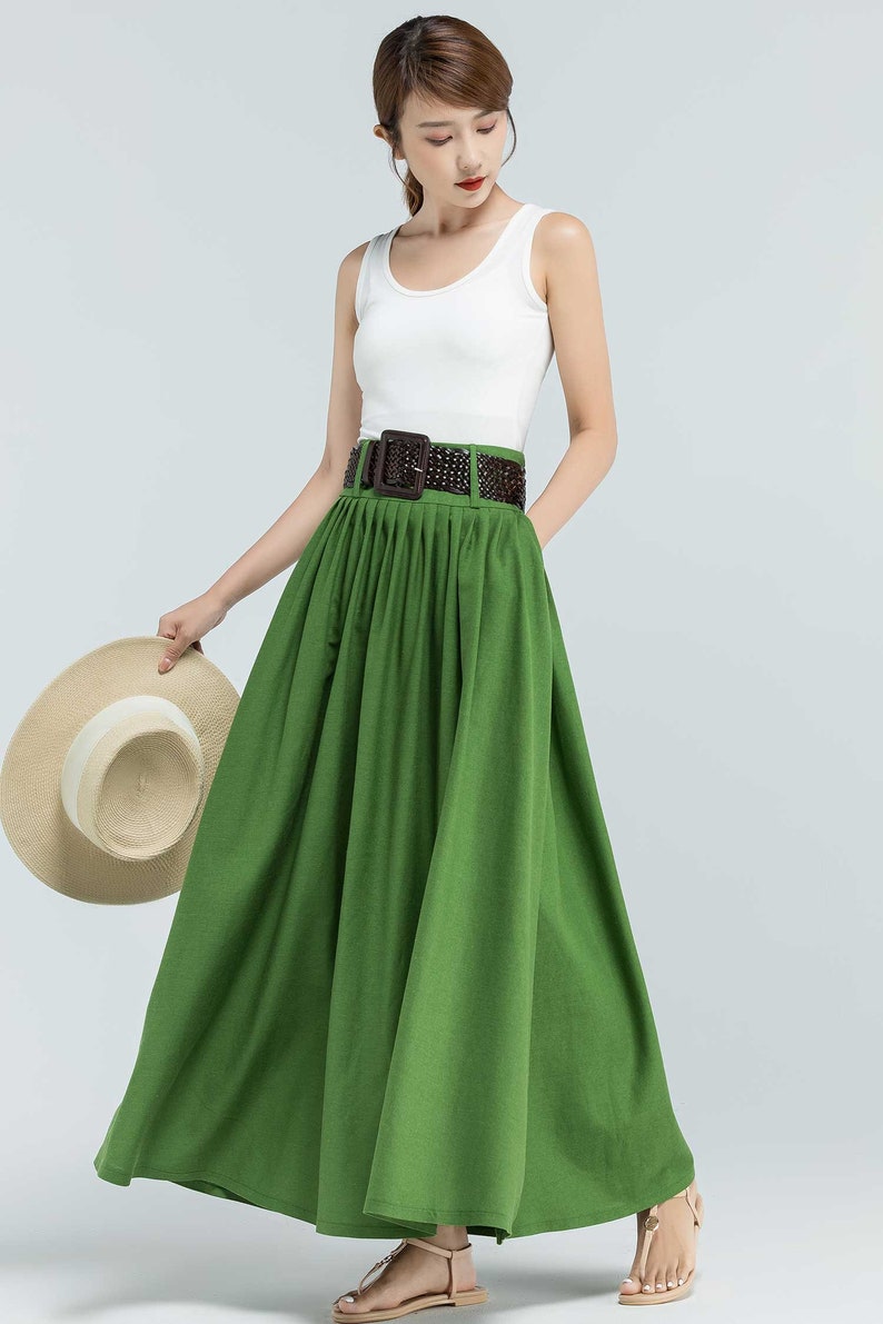 May include: A green maxi skirt with a brown woven belt. The skirt is pleated and has a flowing silhouette.