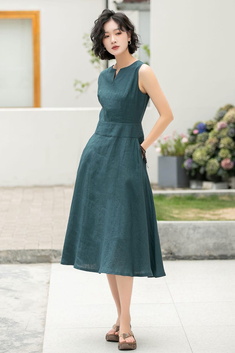 Peut inclure: Une femme portant une robe midi sans manches bleu sarcelle avec un d&eacute;collet&eacute; en V. La robe a un corsage ajust&eacute; et une jupe ample.