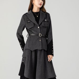 Puede incluir: Una chaqueta gris con cintur&oacute;n negro y falda a juego. La chaqueta tiene cierre de botones y bolsillos de solapa. La falda tiene un dise&ntilde;o de capas y un ribete negro.