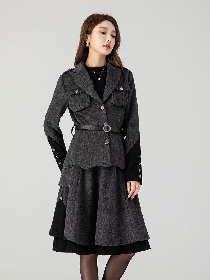 Puede incluir: Una chaqueta gris con cintur&oacute;n negro y falda a juego. La chaqueta tiene cierre de botones y bolsillos de solapa. La falda tiene un dise&ntilde;o de capas y un ribete negro.