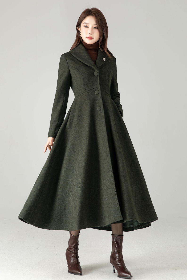 May include: A dark green, long coat with a flared skirt and a tailored bodice. The coat features a notched collar, button closures, and long sleeves. A small brooch adorns the lapel. The coat is a classic style, suitable for formal occasions.