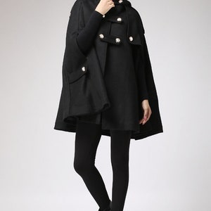 May include: A black hooded cape with a double-breasted button closure and a high collar. The cape is made of a soft, warm fabric and has a relaxed fit.