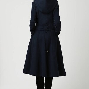 Op de afbeelding: Een marineblauwe capuchonjas met een getailleerde tailleband en een uitlopende rok. De jas heeft een lange, vloeiende silhouet en is perfect voor een stijlvolle winterlook.