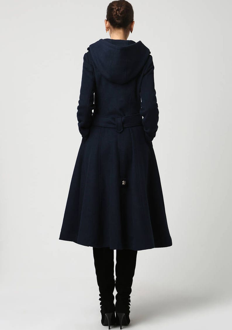 Op de afbeelding: Een marineblauwe capuchonjas met een getailleerde tailleband en een uitlopende rok. De jas heeft een lange, vloeiende silhouet en is perfect voor een stijlvolle winterlook.