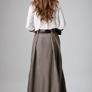 May include: A long, brown skirt with a brown leather belt. The skirt is pleated and has a flowing silhouette.