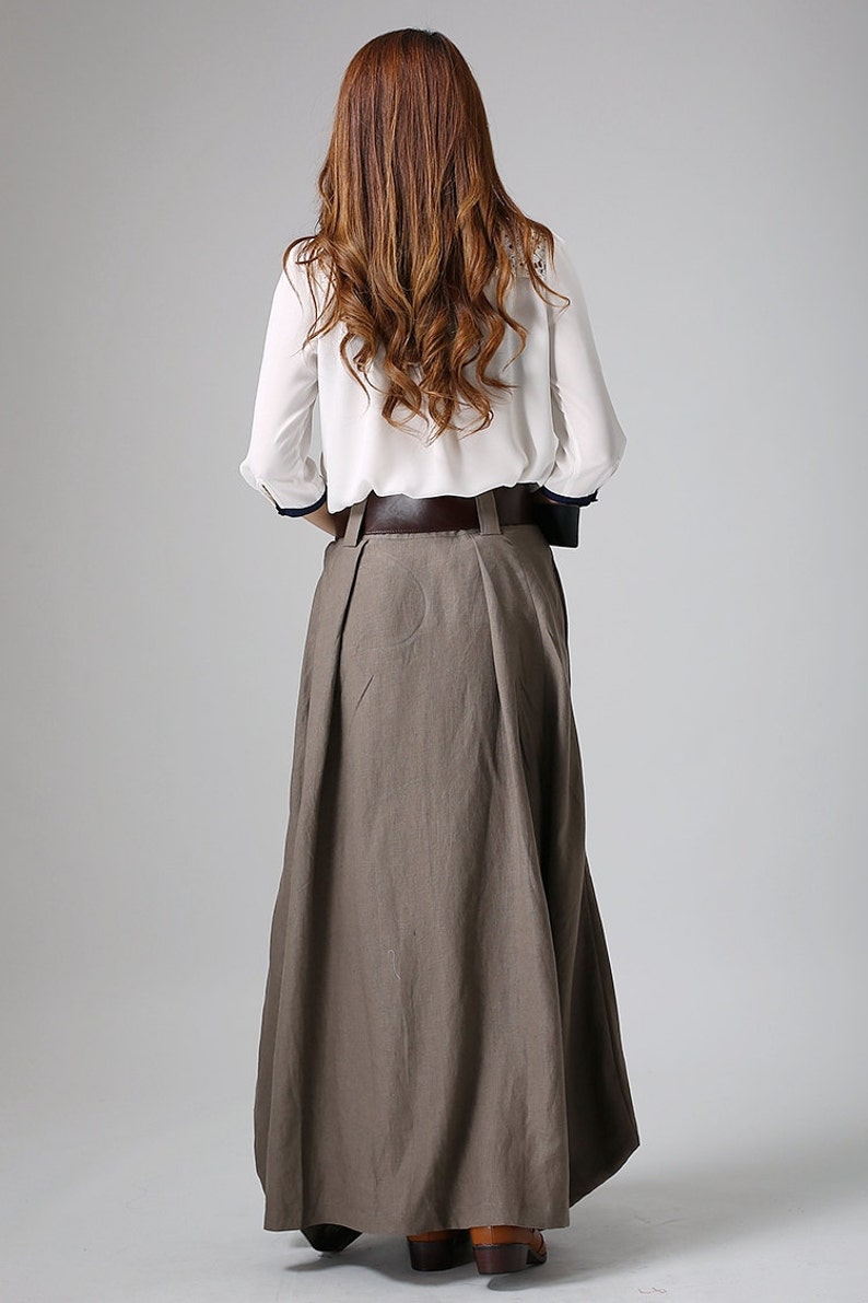 May include: A long, brown skirt with a brown leather belt. The skirt is pleated and has a flowing silhouette.