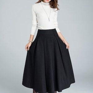 May include: A black midi skirt with a high waist and pleats. The skirt is made of a thick, textured fabric and falls to the mid-calf.