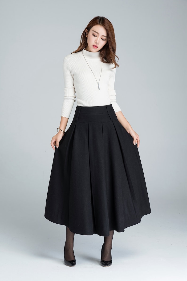 May include: A black midi skirt with a high waist and pleats. The skirt is made of a thick, textured fabric and falls to the mid-calf.