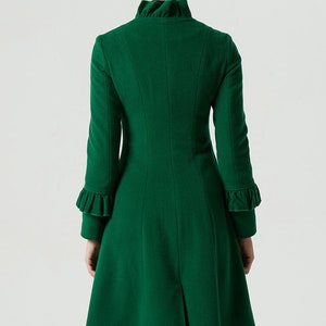 May include: A long, green coat with a ruffled collar and cuffs. The coat has a fitted bodice and a flared skirt.