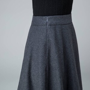 May include: A dark gray skirt with a zipper closure in the back. The skirt is knee-length and has a flared silhouette.