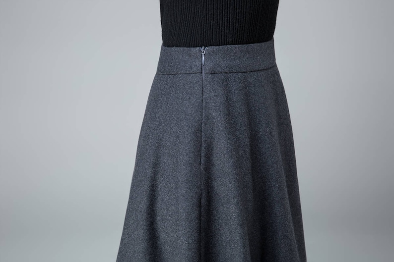 May include: A dark gray skirt with a zipper closure in the back. The skirt is knee-length and has a flared silhouette.