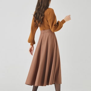 May include: A brown midi skirt with a high waist and a flared silhouette. The skirt is made of a smooth, woven fabric and has a zipper closure in the back.