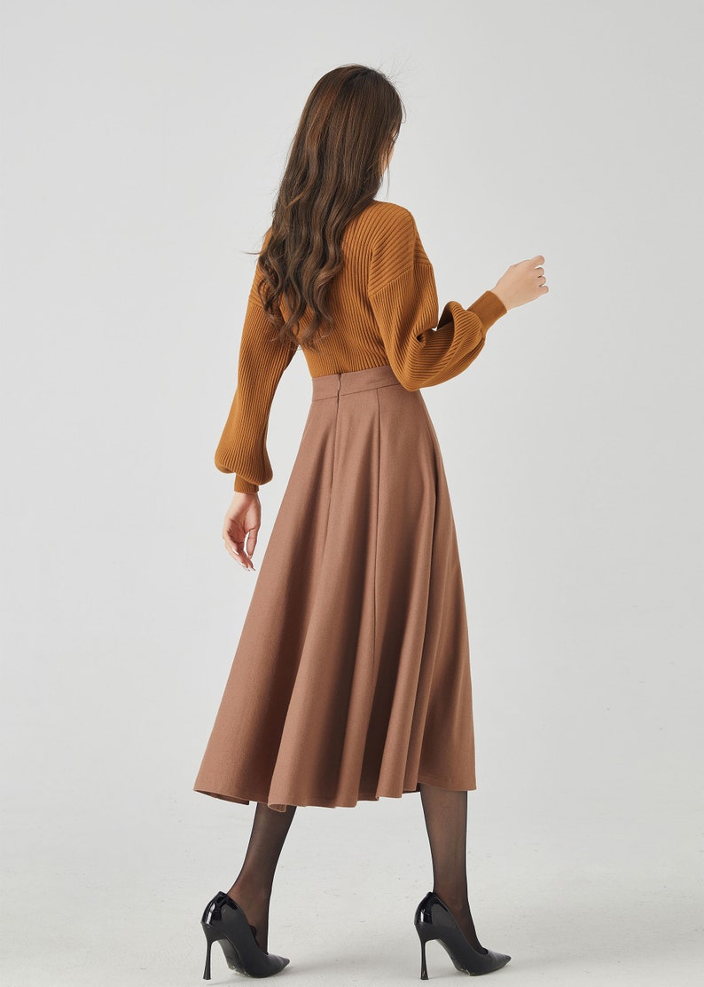 May include: A brown midi skirt with a high waist and a flared silhouette. The skirt is made of a smooth, woven fabric and has a zipper closure in the back.