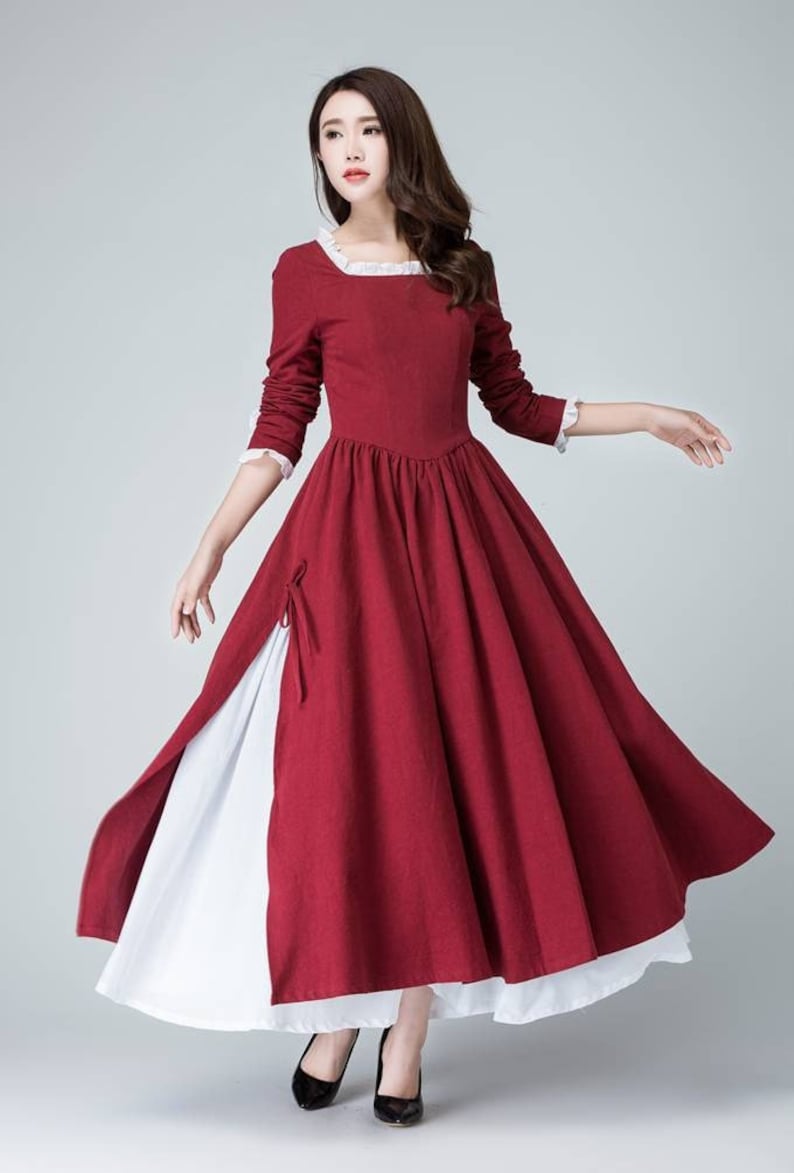May include: A long-sleeved, red dress with a white lace trim around the neckline and cuffs. The dress has a fitted bodice and a full skirt. The skirt has a white underskirt that shows through a slit on the side.