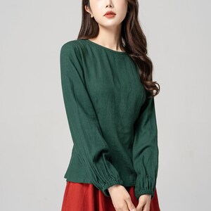 May include: A green long-sleeved shirt with a round neckline and gathered cuffs. The shirt is made of a soft, lightweight fabric and has a relaxed fit.