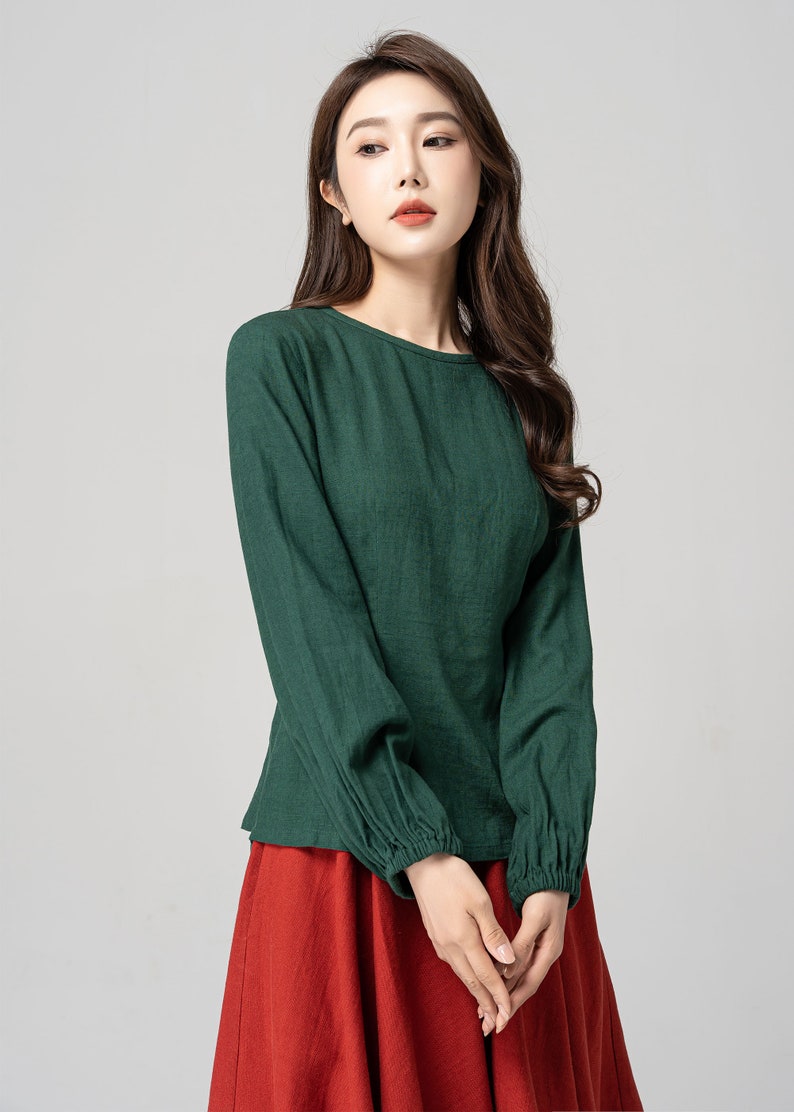 May include: A green long-sleeved shirt with a round neckline and gathered cuffs. The shirt is made of a soft, lightweight fabric and has a relaxed fit.