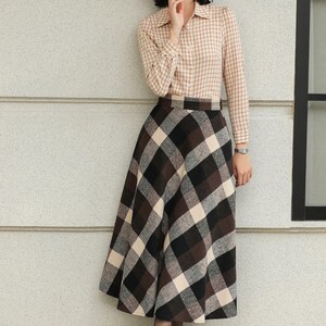 May include: A woman wearing a beige plaid button-down shirt and a long plaid skirt in shades of brown, black, and cream. She is also wearing brown lace-up boots. The outfit is suitable for fall or winter.