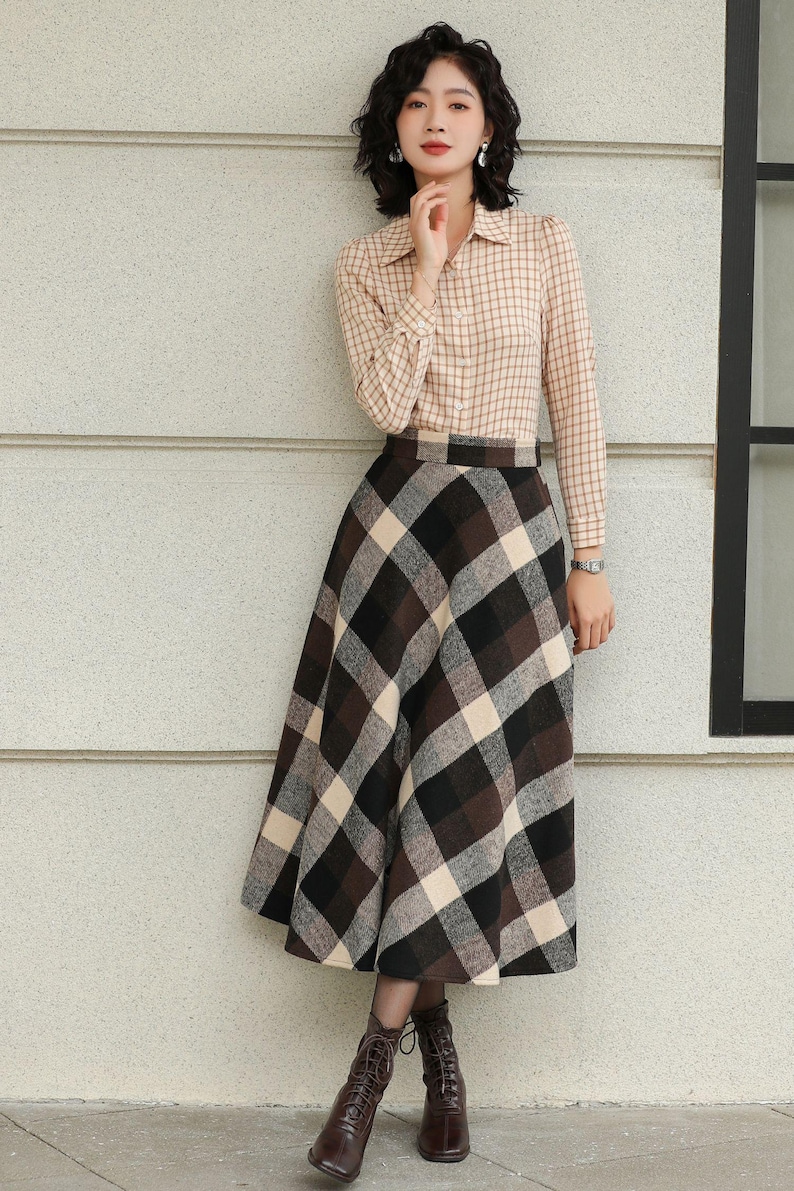 May include: A woman wearing a beige plaid button-down shirt and a long plaid skirt in shades of brown, black, and cream. She is also wearing brown lace-up boots. The outfit is suitable for fall or winter.