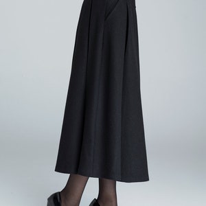 May include: A black high-waisted skirt with pleats and a side pocket. The skirt is made of a thick, textured fabric and falls to the mid-calf.