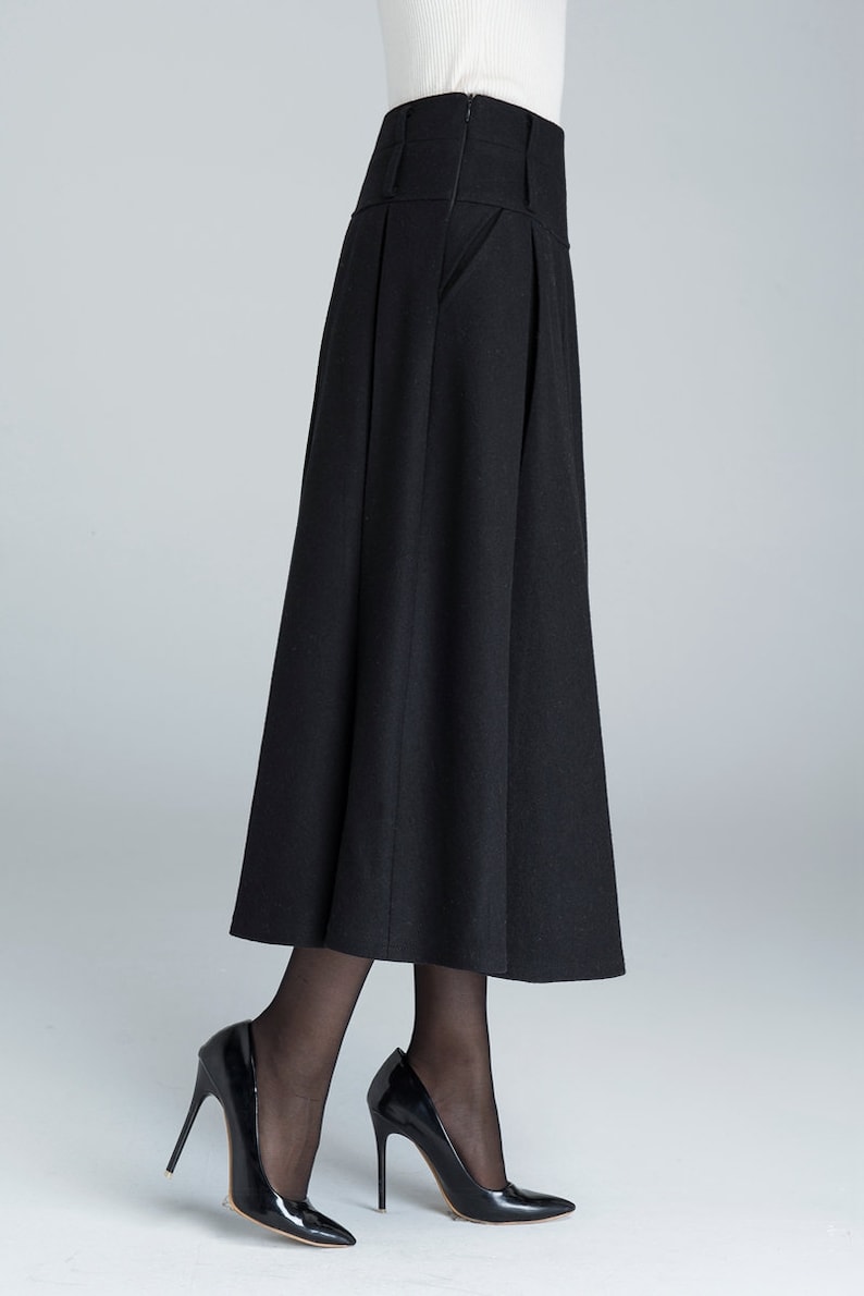 May include: A black high-waisted skirt with pleats and a side pocket. The skirt is made of a thick, textured fabric and falls to the mid-calf.