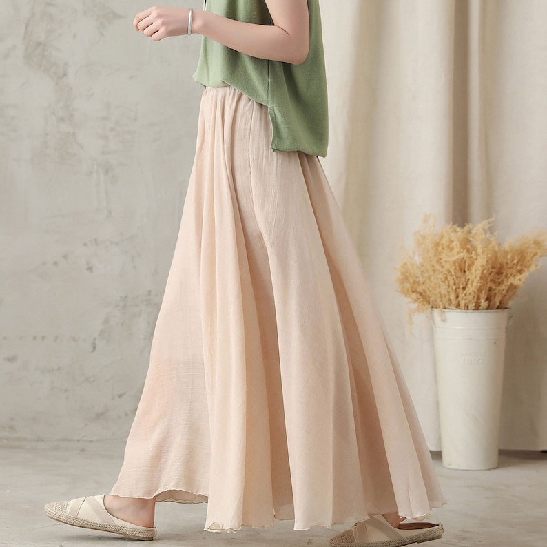 May include: A flowing, light beige maxi skirt. The skirt is paired with a green top. The skirt has a wide, flared design, suggesting a comfortable and breezy fit. The fabric appears to be lightweight, suitable for warmer weather.