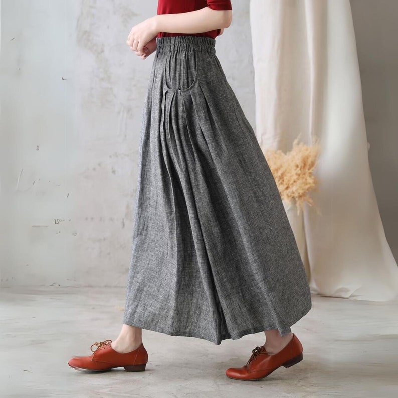 May include: A gray linen skirt with a pleated front and a single pocket on the left side. The skirt has an elastic waistband and falls to the ankles.