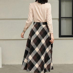 May include: A long-sleeved, tan plaid shirt paired with a brown, black, and cream plaid skirt. The skirt is a midi length. Brown ankle boots complete the outfit. The outfit is suitable for fall or winter.
