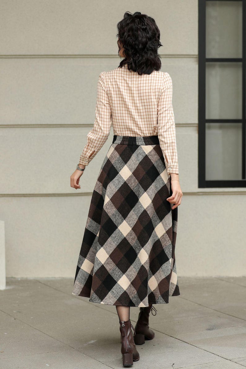 May include: A long-sleeved, tan plaid shirt paired with a brown, black, and cream plaid skirt. The skirt is a midi length. Brown ankle boots complete the outfit. The outfit is suitable for fall or winter.