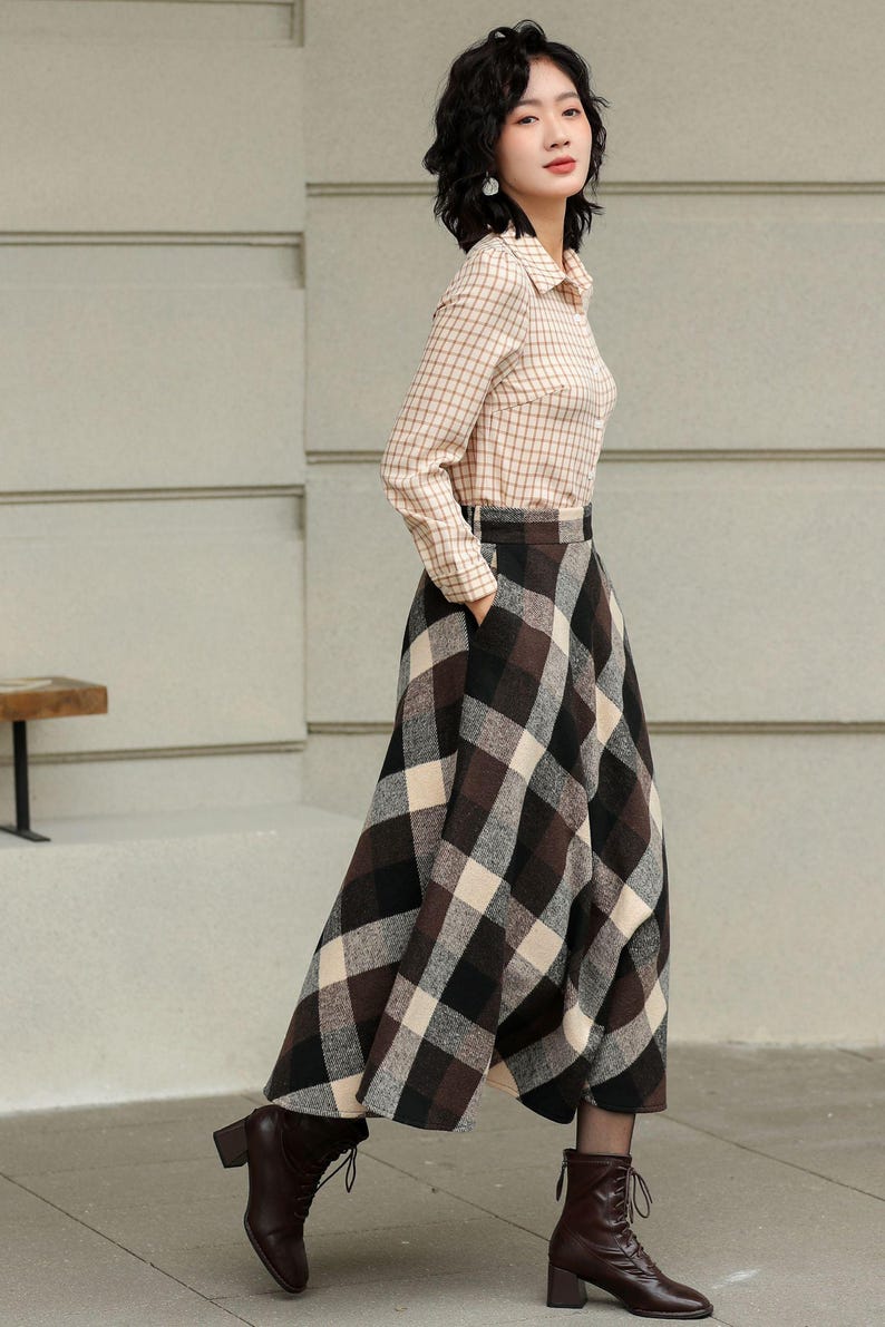 May include: A woman wearing a beige plaid button-down shirt and a long, brown, black, and cream plaid skirt. She is wearing dark brown lace-up boots. The outfit is a classic, stylish ensemble.