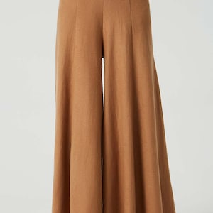 May include: Wide-leg, high-waisted pants in a brown color. The pants have a relaxed fit and a flowing silhouette.