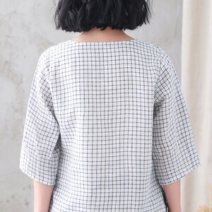 Op de afbeelding: Een wit en blauw geruit blouse met een vierkante halslijn en driekwart mouwen.