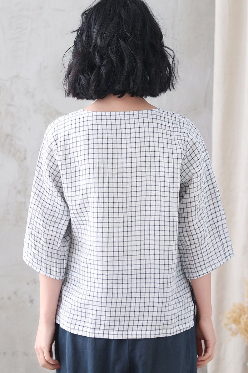 Op de afbeelding: Een wit en blauw geruit blouse met een vierkante halslijn en driekwart mouwen.