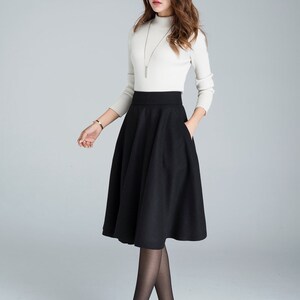 Peut inclure: Une jupe midi noire &agrave; taille haute avec une silhouette &eacute;vas&eacute;e. La jupe a un design simple avec deux poches sur le devant.